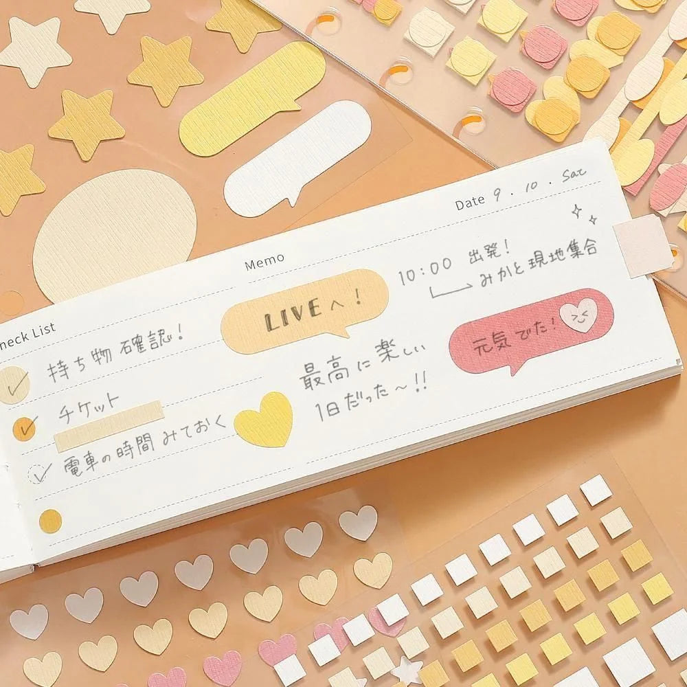 A white notebook or planner page with cute pastel stickers and handwritten notes, surrounded by matching star, heart, and square stickers on a peach-colored surface, showing the possible uses of Daily Palette stickers by BGM Life. 